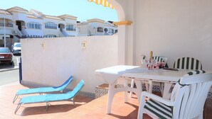 A patio with a table and chairs, a sun lounger, and a view of buildings in the background. - 001 - Altomar II 001 - comfortHOLIDAYS (Santa Pola)