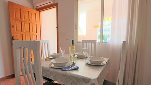 A dining area with a table set for four, white chairs, and a window with curtains. - 001 - Altomar II 001 - comfortHOLIDAYS (Santa Pola)