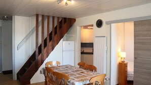 Uma área de refeições com mesa e cadeiras de madeira, uma escada, uma cozinha e um relógio na parede.