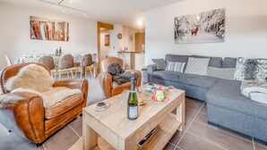 A modern living room with a sofa, a coffee table, and a dining area with a table and chairs. - 4* Apartment at Slopeside, Sleeps 8, Wi-Fi Included (Champagny-en-Vanoise)