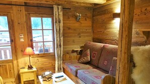 A wooden cabin interior with a sofa, a table, a lamp, and a mounted animal head.
