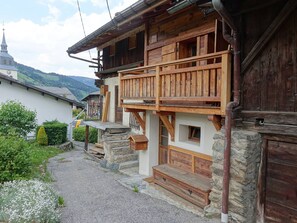 Une maison traditionnelle en bois, avec des fondations en pierre, un balcon en bois et une allée gravillonnée.