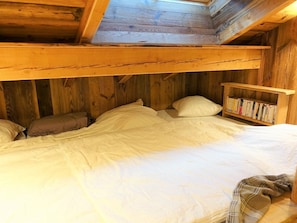 A wooden cabin bedroom with a bunk bed, a bookshelf, and a skylight.