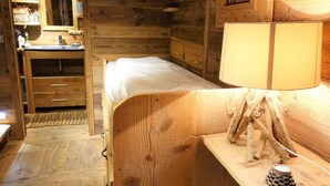 A wooden cabin-style room with a bed, a dresser, a mirror, and a lamp.