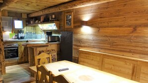 A wooden interior with a dining table, chairs, a kitchen area with appliances, and a television.