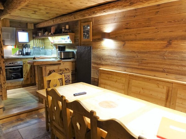 Un intérieur en bois comprenant une table à manger, des chaises, un coin cuisine avec des appareils électroménagers et un téléviseur.