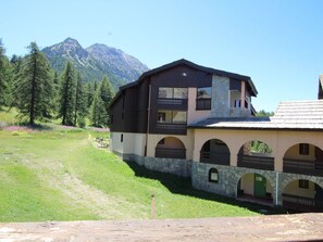 A two-story building with a stone base and a dark upper section, set against a mountainous backdrop.