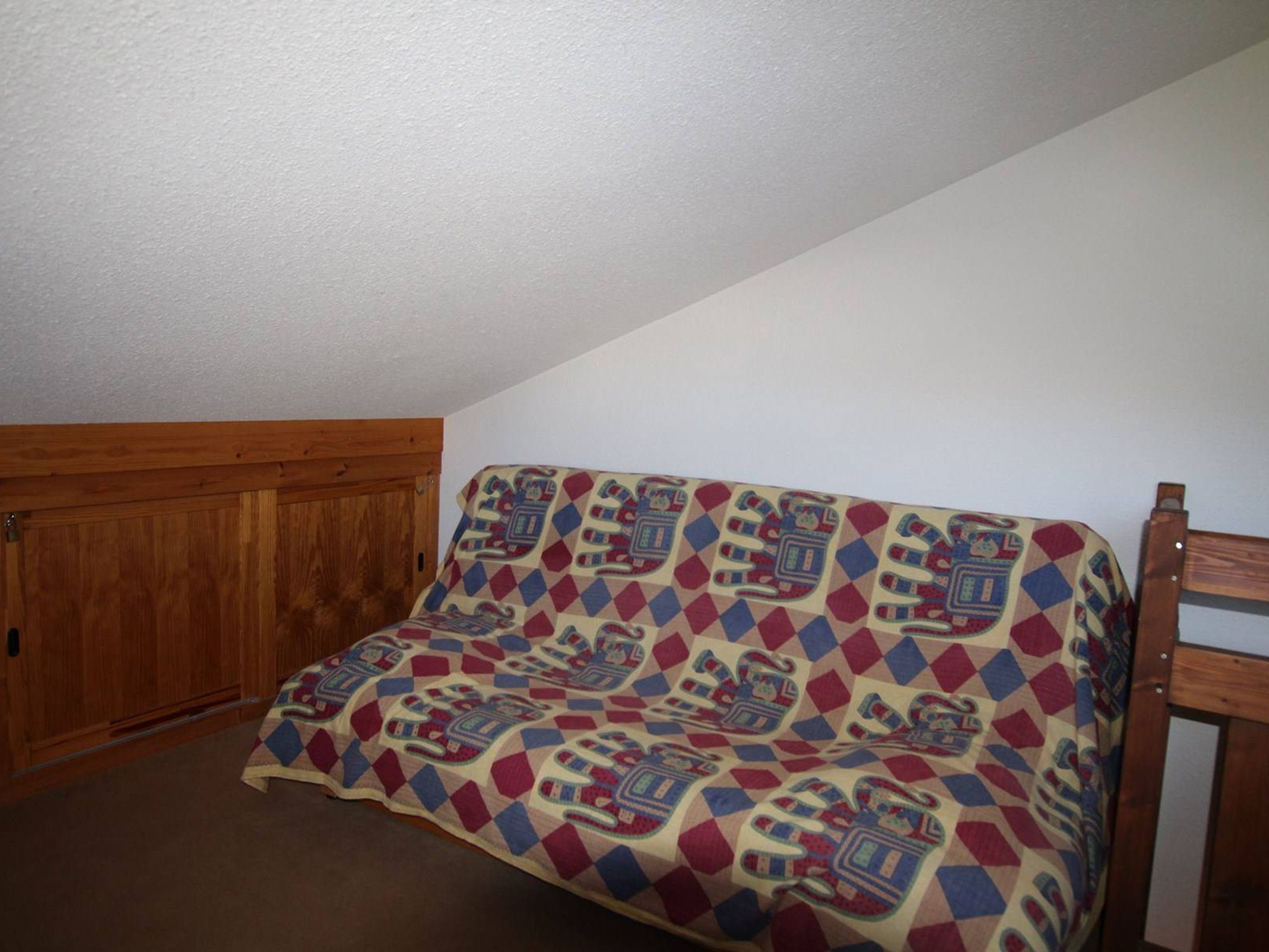 Una habitación de esquina con un armario de madera, un edredón estampado sobre un sofá y una silla de madera.