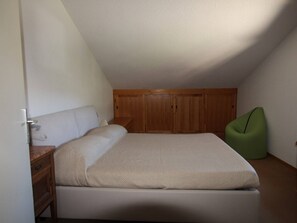 Une chambre à coucher avec un lit, une armoire en bois et un fauteuil en forme de haricot vert.