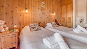 Ein Zimmer mit Holzwänden, zwei Betten, einem Nachttisch und zwei Teddybären, ein großer davon ist weiß.