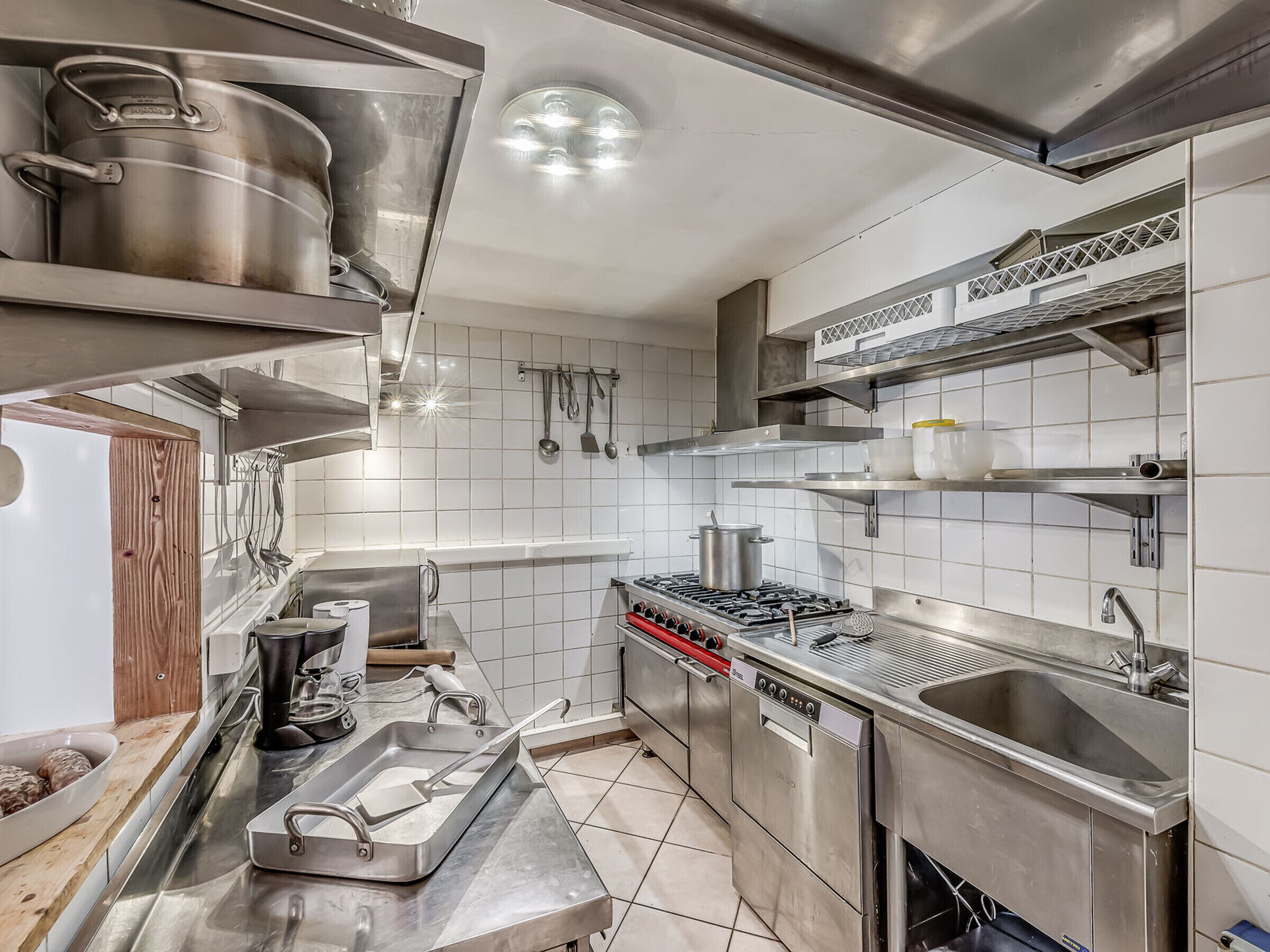 A modern kitchen with stainless steel appliances, white tiled walls, and a variety of utensils hanging on the wall.