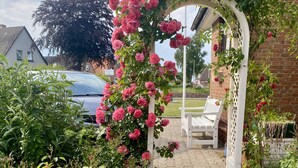 A garden with a white archway covered in pink roses, a gravel path, and a white chair.