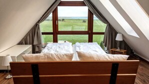 A bedroom with a wooden bed, a desk, and a window with a view of a green field.