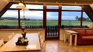 A dining area with a table, chairs, and a view of a field through large windows.