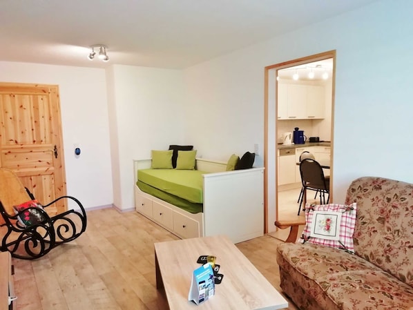 A compact living space with a bed, a sofa, a dining table, and a kitchenette.