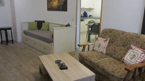 Ein kleiner, gemütlicher Wohnraum mit einer Couch, einem Holztisch und einem Essbereich, der durch eine offene Tür sichtbar ist.