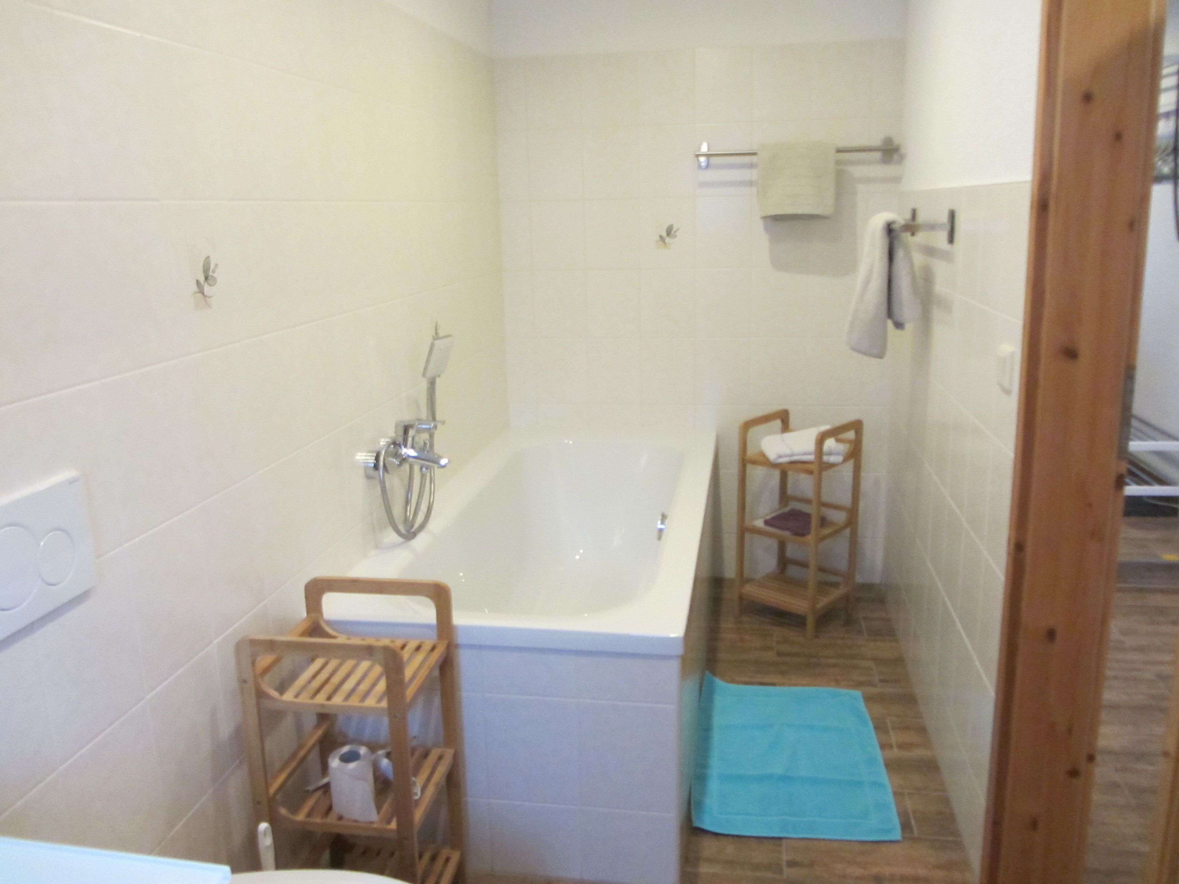 A small bathroom with a bathtub, a wooden shelf, and a blue towel on the floor.