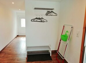 A hallway with a white door, a coat rack with black hangers, a green basket, and a red and white folding chair.