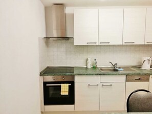 A kitchen with white cabinets, a stainless steel range hood, a built-in oven, a sink, and a kettle.