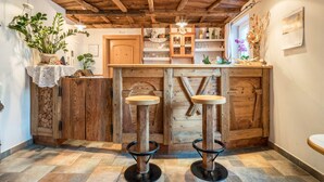 A rustic bar area with wooden stools, a wooden counter, and a stone wall. - Comfortable Apartment “Treyer 3 Typ B” with Mountain View, Balcony & Garden (Terenten / Pustertal)