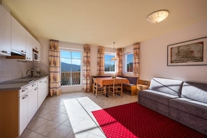Un espacio habitable compacto con kitchenette, comedor, sofá y ventana con cortinas.