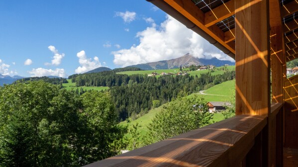 Varanda de madeira com vista para uma paisagem montanhosa, casas e vegetação.