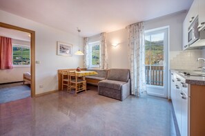 A compact living space with a dining area, a sofa, a kitchen with a stove, and a view of the outdoors.