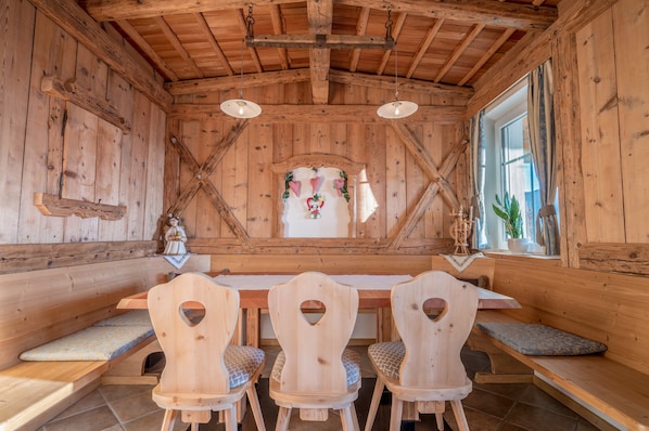 A wooden interior with a wooden table and chairs, a window with curtains, and a decorative wall piece.
