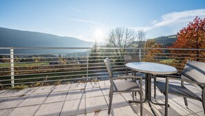 Eine Terrasse mit Tisch und Stühlen mit Blick auf eine malerische Landschaft, Berge und ein Gewässer.