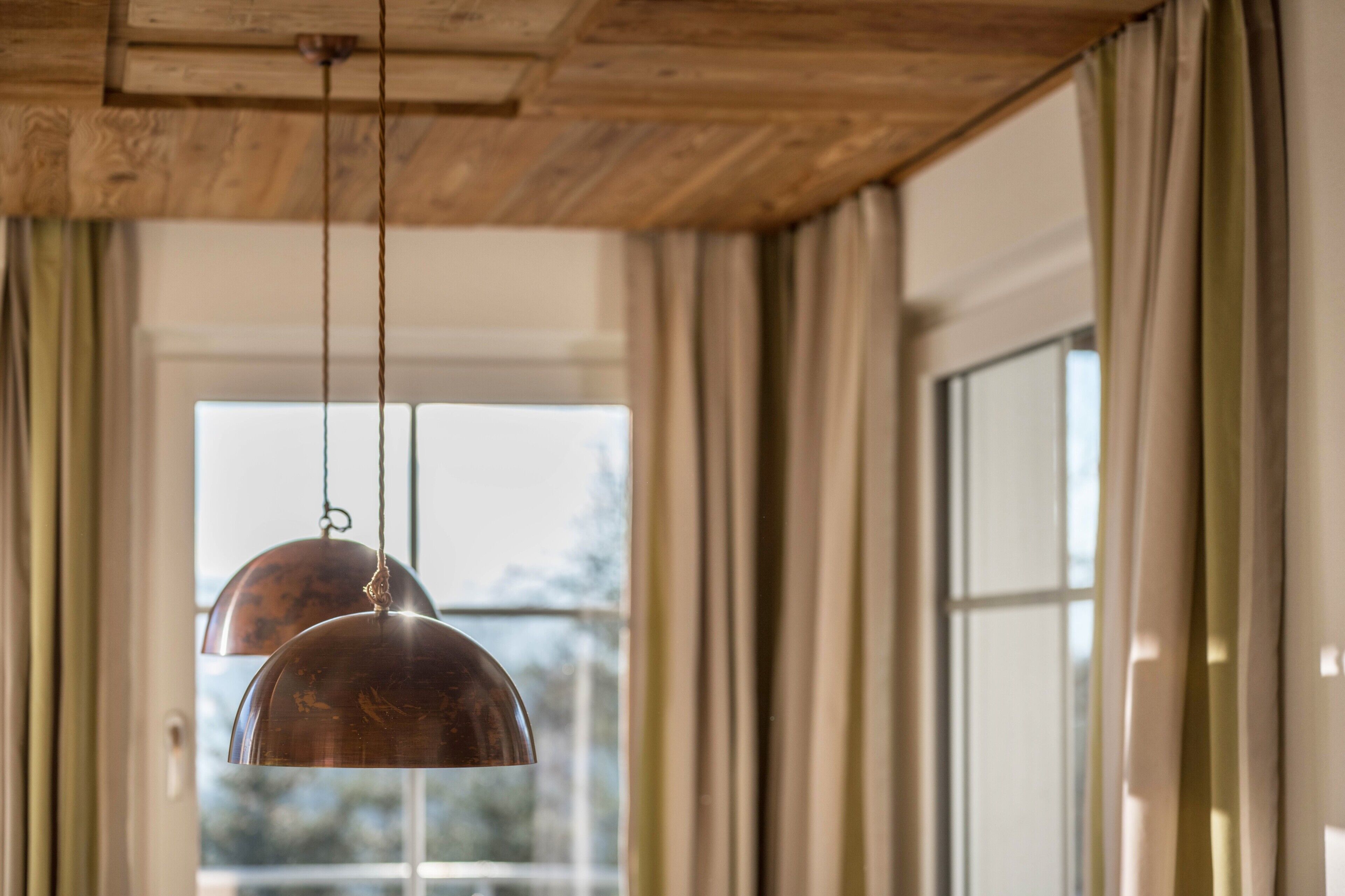 A room with a wooden ceiling, large windows, and hanging copper pendant lights.