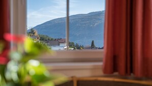 A view through a window with curtains, featuring a mountain and a building in the background. - Apartment “Treyer 1 Typ B” with Mountain View, Wi-Fi, Balcony & Garden (Terenten / Pustertal)
