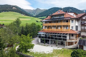 Un edificio de varios pisos con balcón, paneles solares y vistas a un valle verde y montañas.