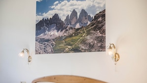 Ein Schlafzimmer mit einem Holzkopfteil, einem Berglandschaftsbild und zwei Wandleuchten.