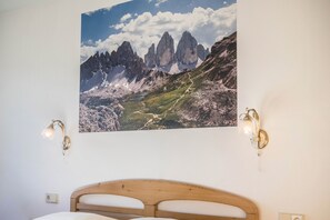 A bedroom with a wooden headboard, a mountain landscape painting, and two wall-mounted lights.
