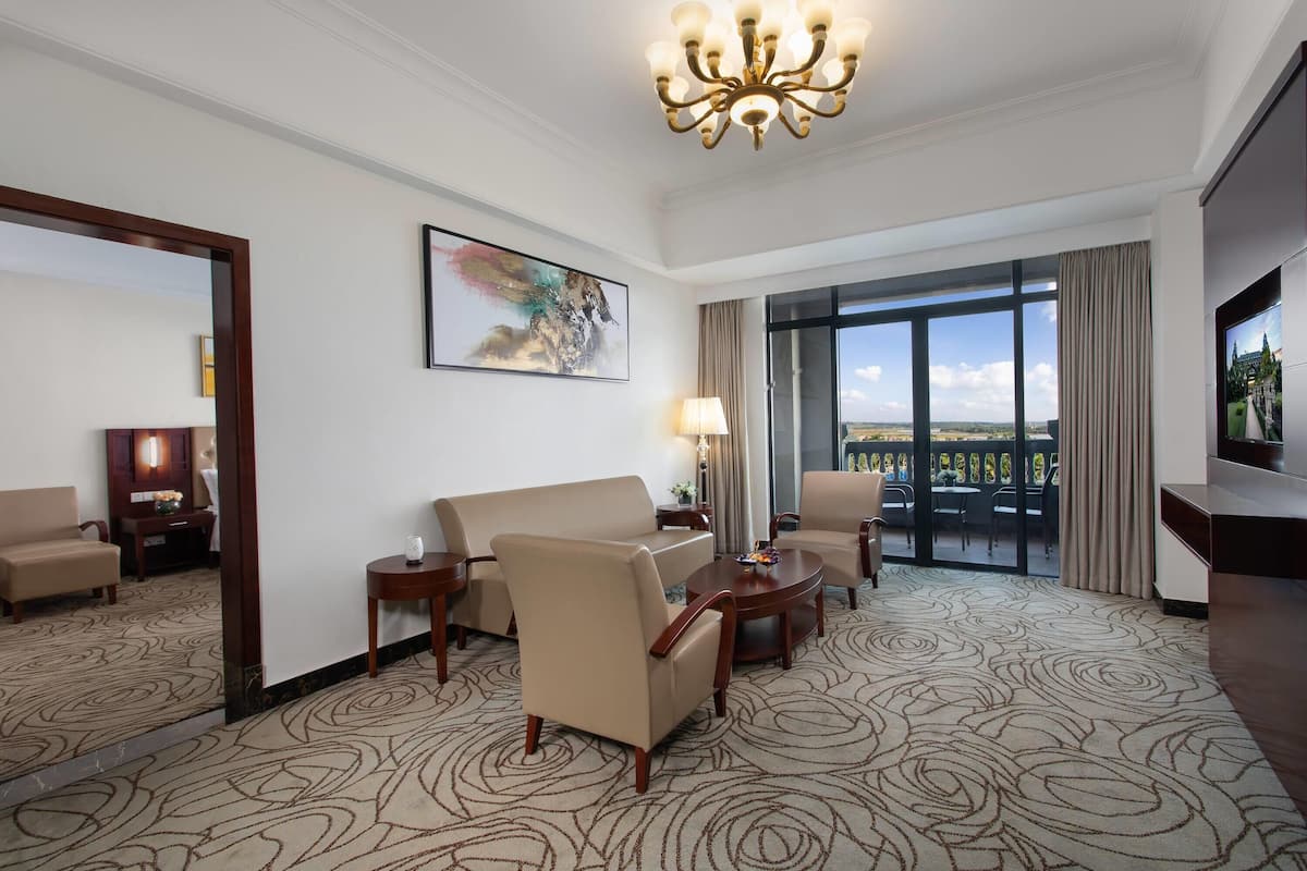 A hotel room with a large window, a chandelier, a sofa, a chair, and a TV.