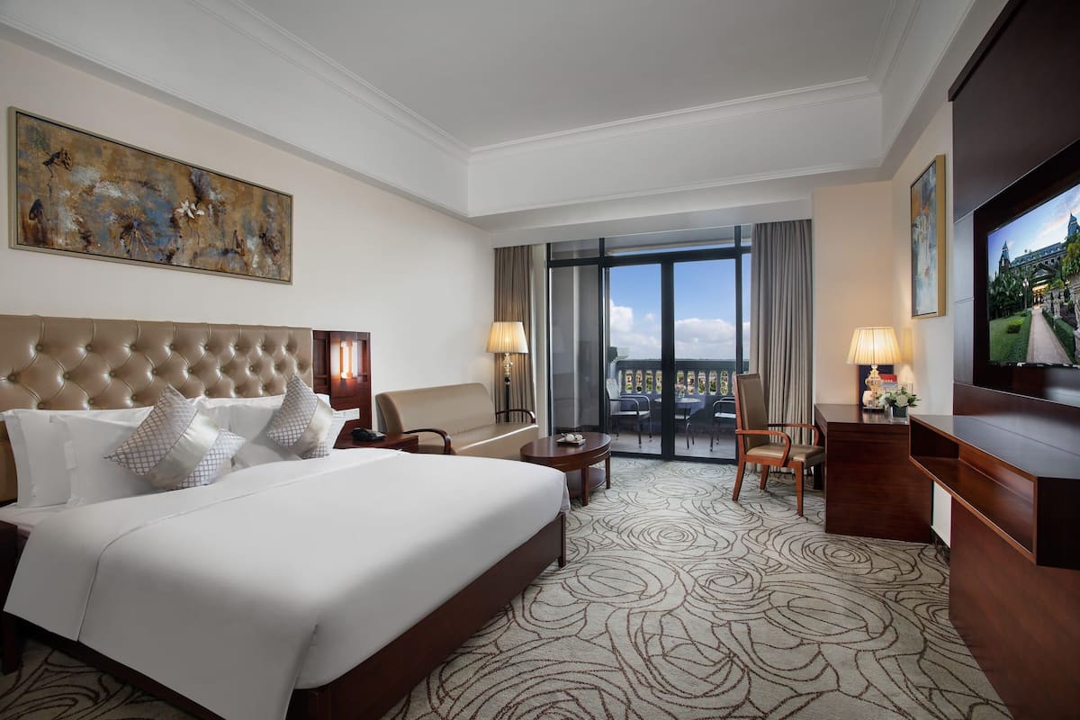 A hotel room with a large bed, a desk, a television, and a view of the city.