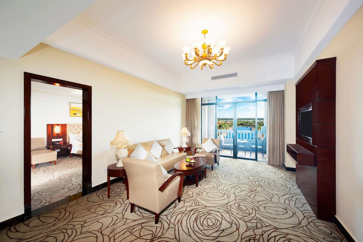 A hotel room with a large bed, a sitting area with a sofa and armchairs, a television, and a view of the outdoors.