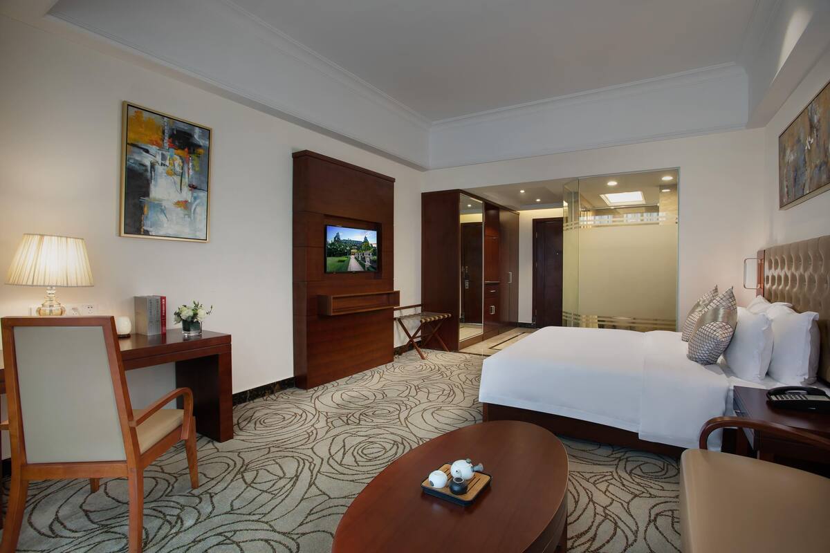 A hotel room with a bed, a desk, a chair, a TV, and a coffee table.