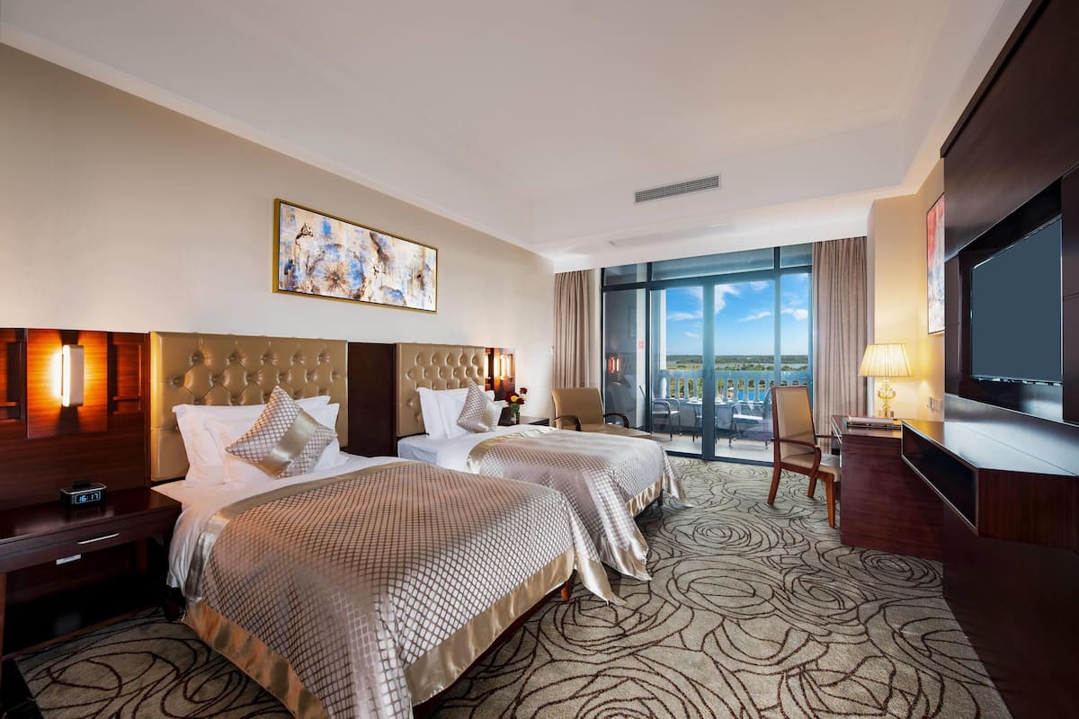 A hotel room with two beds, a large window with a view, a TV, and a desk with a lamp.