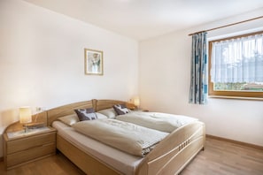 A double bed with a wooden headboard, bedside tables with lamps, a framed picture on the wall, and a window with curtains.
