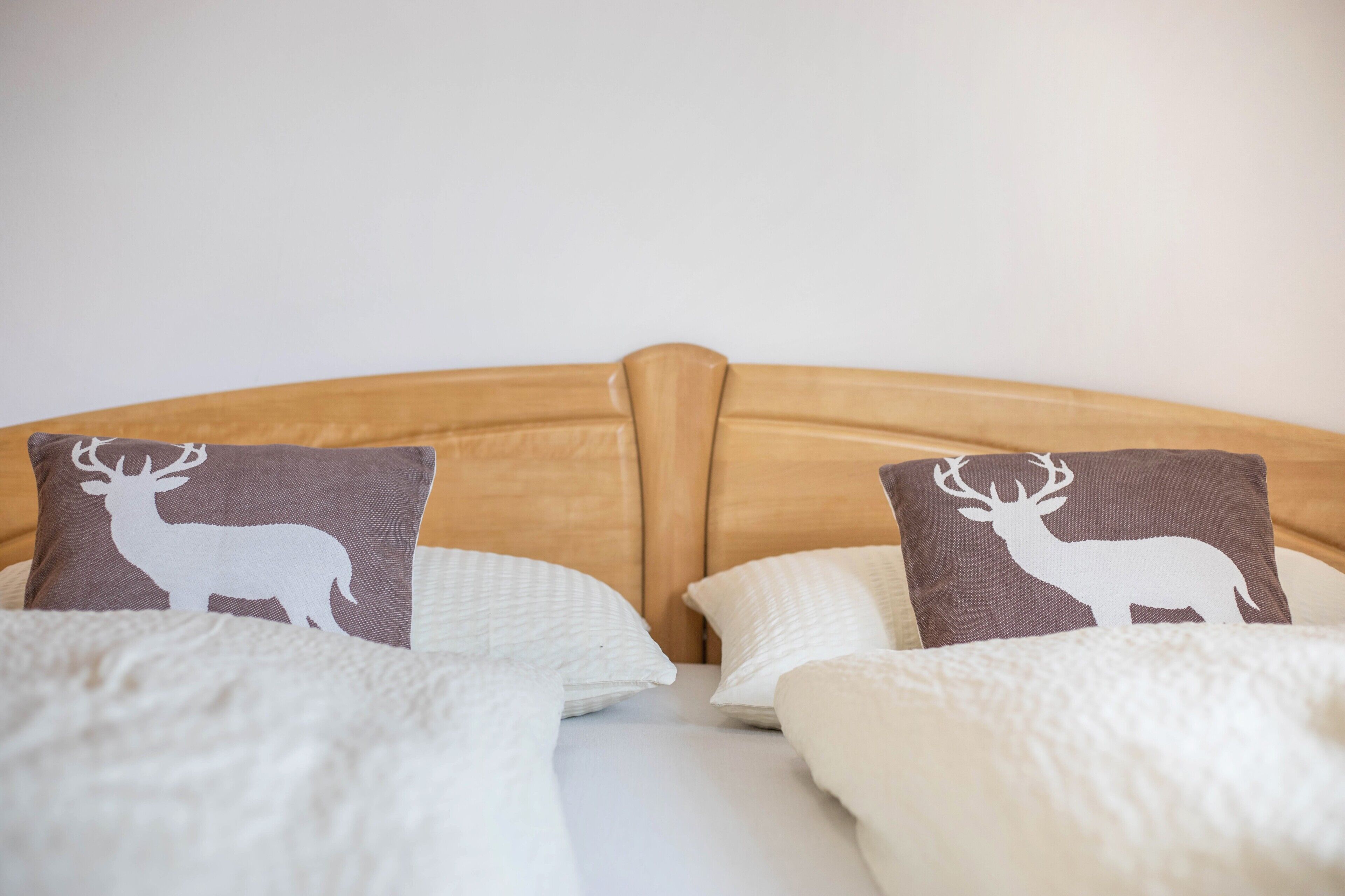 Een bed met twee kussens, met een wit silhouet van een herten en een houten hoofdbord, en witte beddengoed.