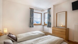 A bedroom with two beds, a dresser, a mirror, and a window with curtains.