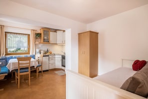 A compact room with a kitchenette, a dining area with a blue sofa, and a bed with a red pillow. - Holiday Apartment A in House Belodei with Mountain View & Wi-Fi; Parking Available (San Martino in Badia)