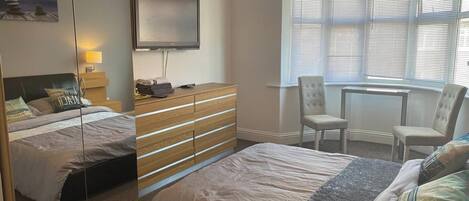 A bedroom with a bed, dresser, mirror, TV, and a window with blinds.