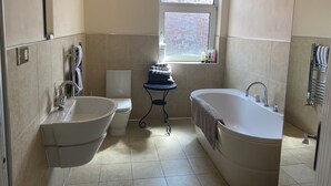 Ein modernes Badezimmer mit einer Badewanne, einer Toilette und einem Waschbecken. Ein Fenster sorgt für natürliches Licht und einen Ausblick nach draußen.