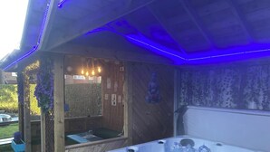 Ein Whirlpool mit Wasserstrahlen, umgeben von einer Holzterrasse und blauer LED-Beleuchtung.