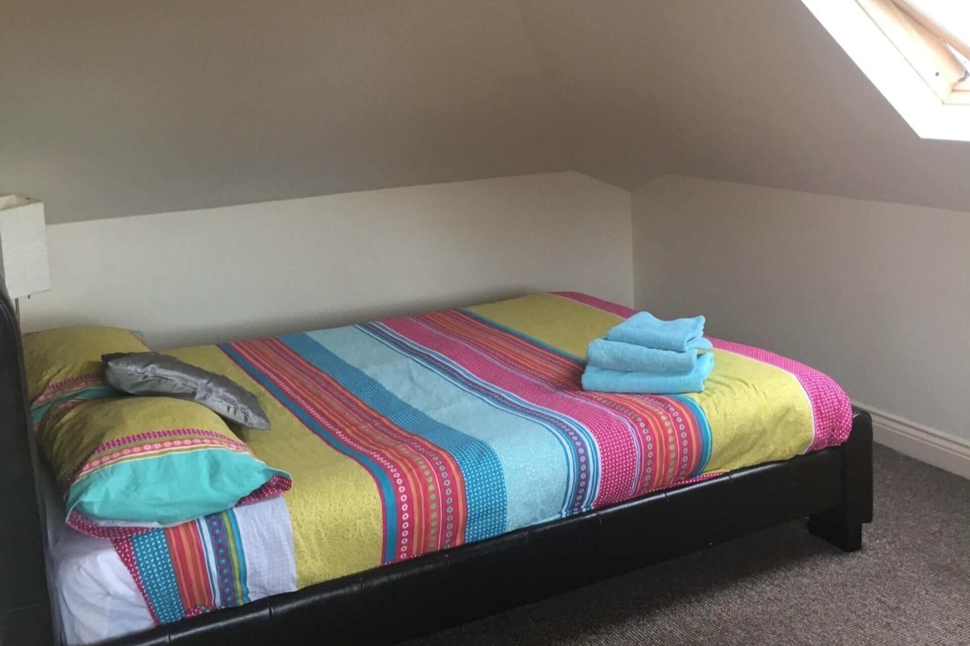A small, single-bed room with a sloped ceiling and a skylight.
