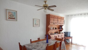 A dining area with a wooden table, chairs, a ceiling fan, and a cabinet with kitchen items. - Beautiful apartment facing the sea (Mont-roig del Camp)