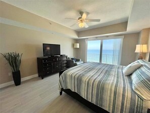 A bedroom with a bed, a TV on a dresser, a potted plant, and a view of the ocean. - 902 Sanibel - Oceanfront Panoramic Views (Daytona Beach Shores)