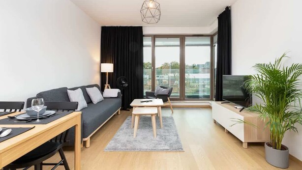 Moderni olohuone, jossa on sohva, ruokapöytä, televisio ja suuri ikkuna.